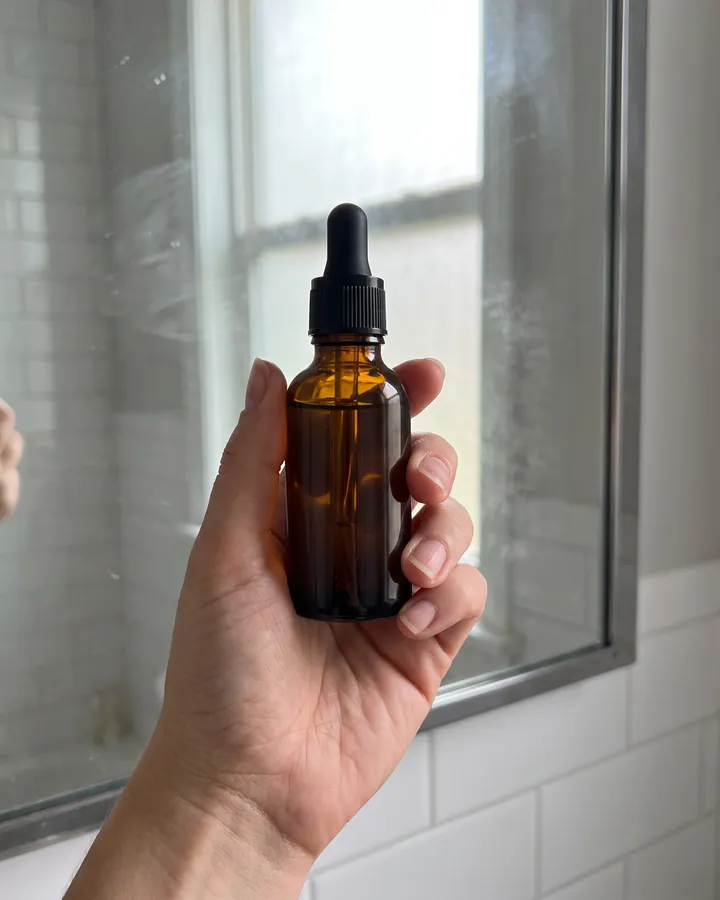 A hand holding the bottle at a steamy mirror.